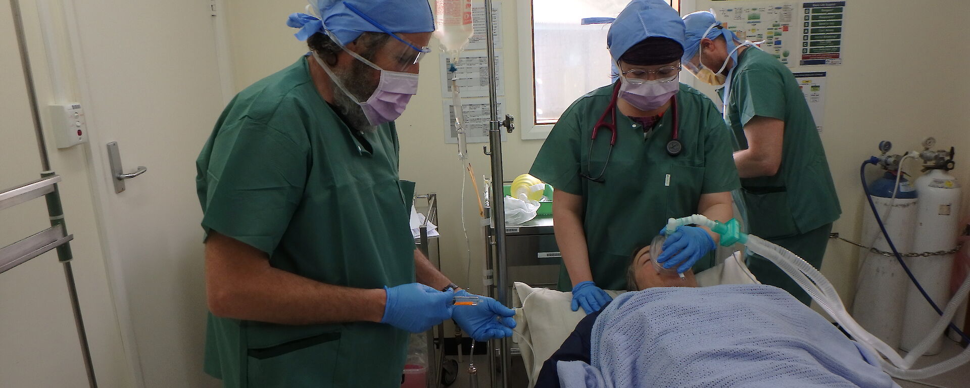 Three medical personnel and one patient lying in a bed