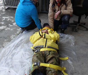 Two exepditioners crouching by the head of a man strapped to a stretcher with a splint on his leg