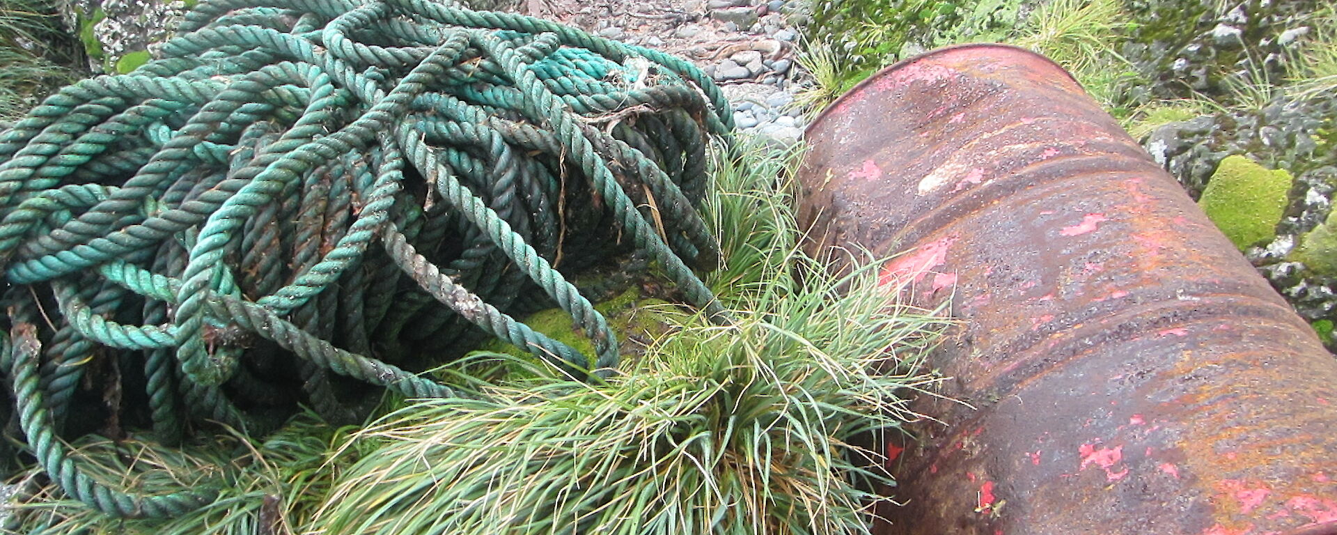 long, rolled up rope and rusty oil drum on the shore