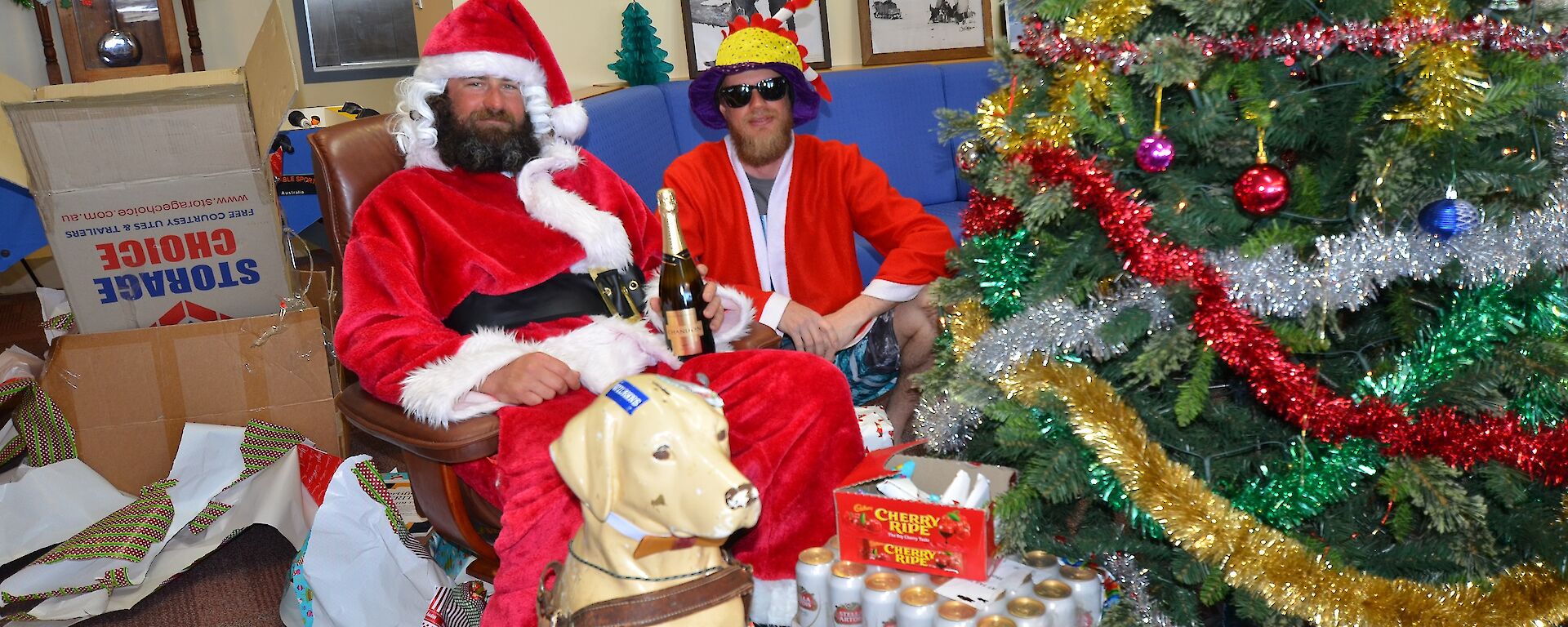 Two men sitting next to a Christmas tree