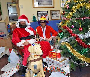 Two men sitting next to a Christmas tree