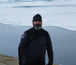Man standing at the edge of the coast with water and icesheets behind him