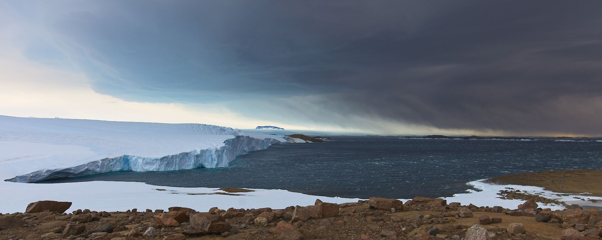 Landscape view of sea ice, ocean, snow covered rocks, and clouds in the sky