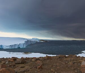 Landscape view of sea ice, ocean, snow covered rocks, and clouds in the sky