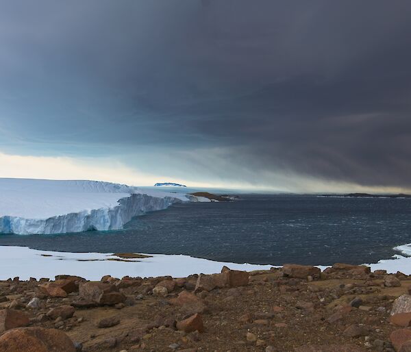 Landscape view of sea ice, ocean, snow covered rocks, and clouds in the sky