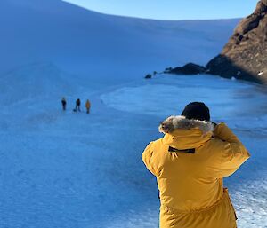 An expeditioner taking a photo of three others down a valley of ice