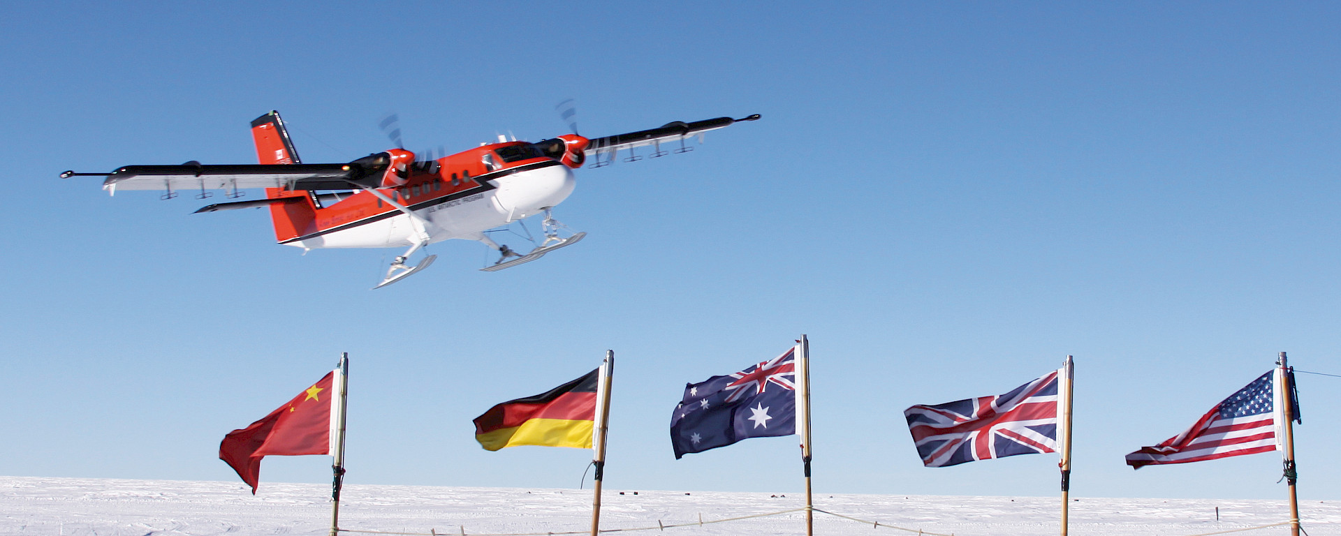 A Twin Otter flies over flags, planted in the ice, of countries participating in a geophysical research project.