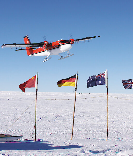 A Twin Otter flies over flags, planted in the ice, of countries participating in a geophysical research project.