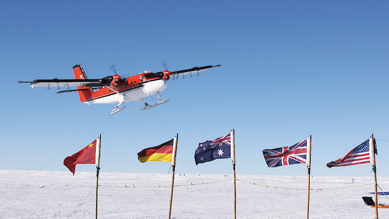 A Twin Otter flies over flags, planted in the ice, of countries participating in a geophysical research project.