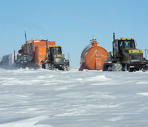 Two tractors tow sleds carrying containers and fuel drums in Antarctica.