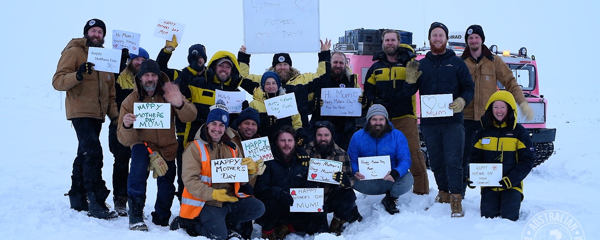 A group of expeditioners in the snow, holding up hand-written Happy Mother’s Day signs