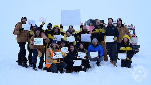 A group of expeditioners in the snow, holding up hand-written Happy Mother’s Day signs