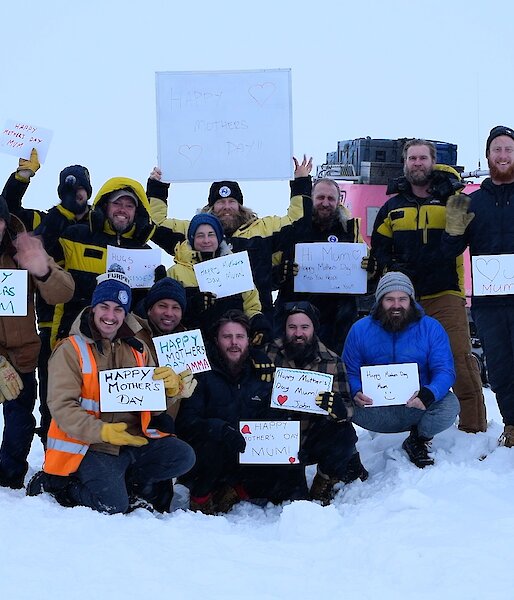 A group of expeditioners in the snow, holding up hand-written Happy Mother’s Day signs