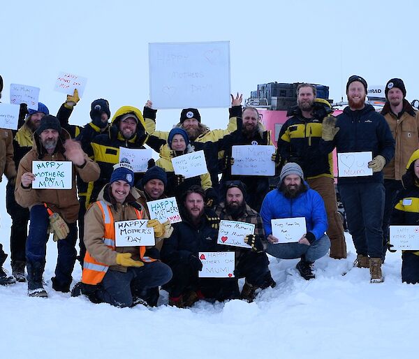 A group of expeditioners in the snow, holding up hand-written Happy Mother’s Day signs