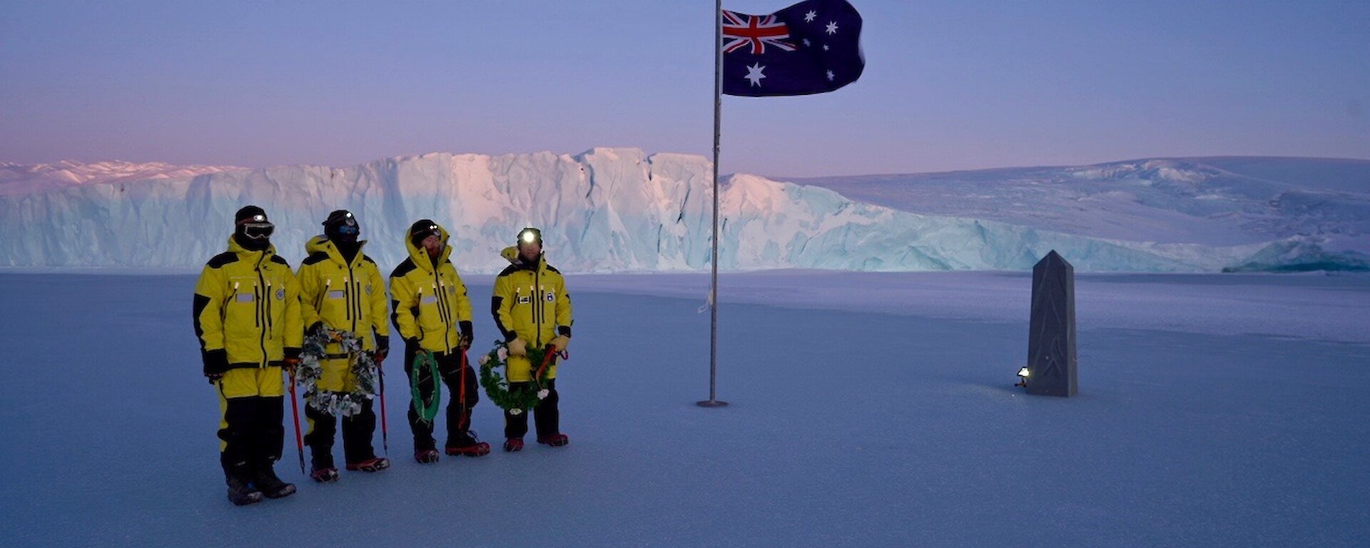 people stand on sea ice with cliff in background