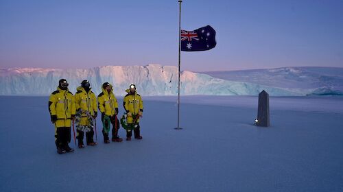people stand on sea ice with cliff in background