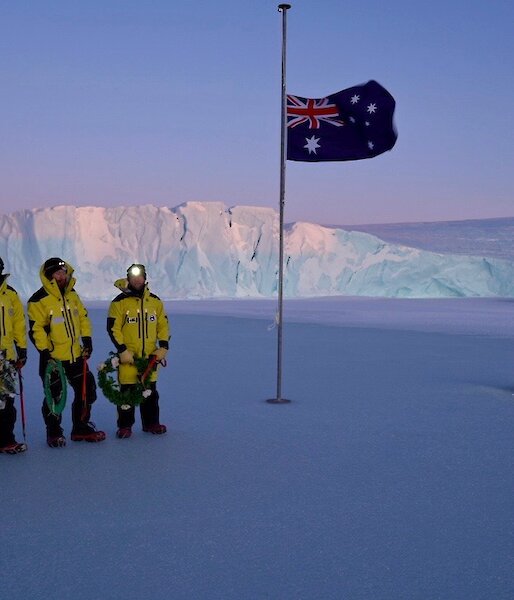 people stand on sea ice with cliff in background