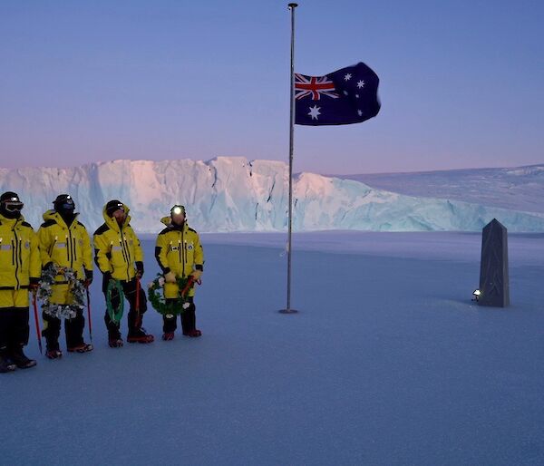 people stand on sea ice with cliff in background