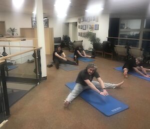 Five expeditioners stretching on the ground while sitting on foam mats