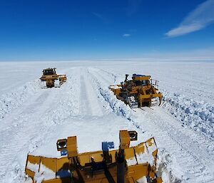 Heavy machinery bulk pushing snow to keep the edges of the blue ice runway clear of obstructions