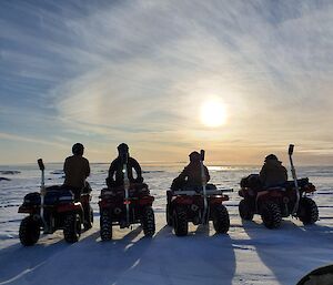 Four expeditioners on quad bikes looking into the sun