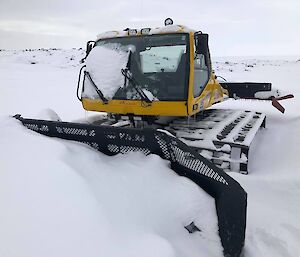 A snow groomer surrounded by blown snow accumulation