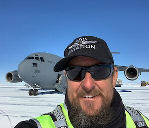 A self portrait of an expeditioner with a large aircraft in the background at the ice runway