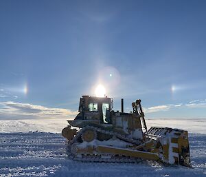 A dozer on the ice with sun dogs, or bright spots, on either side of the sun