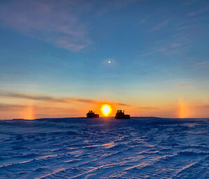Sun setting between two groomers with faint sun dogs, or bright spots, on either side