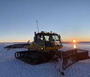 A groomer on the ice with the sun setting in the background