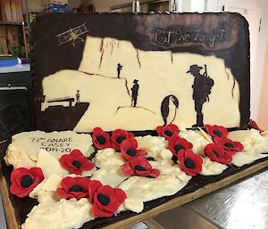 A chocolate ANZAC picture carved in white and dark chocolate with an Antarctic flavour. In front are red icing poppies on while chocolate ice