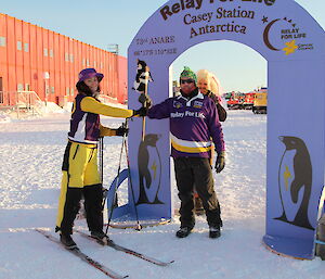 An expeditioner hands a baton over to another expeditioner after coming through the purple Relay For Life arch