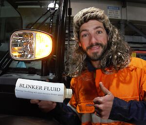 Expeditioner wearing a mullet wig holding a plastic bottle and giving a thumbs up