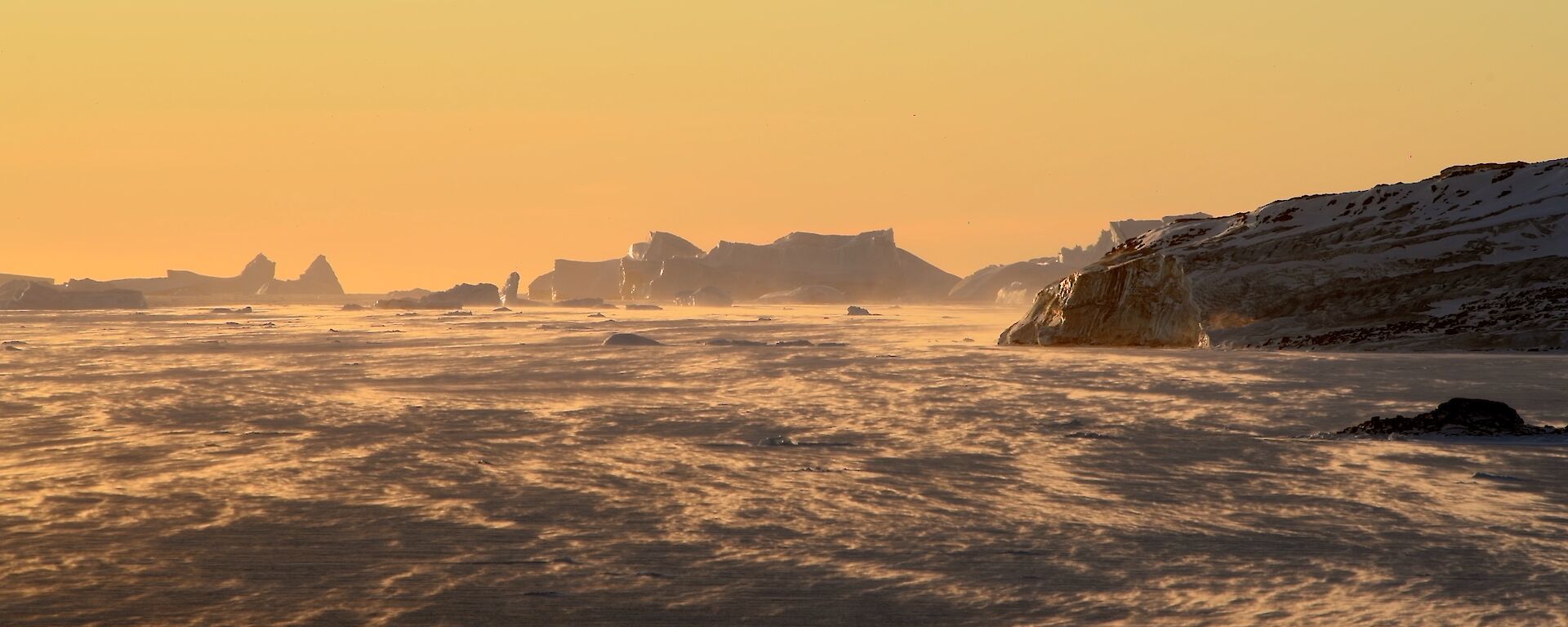 blowing snow bathed in a warm orange glow by the setting sun