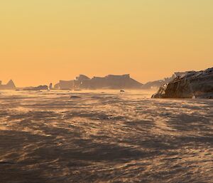 blowing snow bathed in a warm orange glow by the setting sun