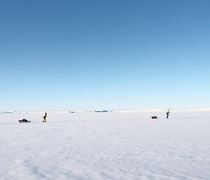 Two expeditioners ski across the white snow covered sea ice pulling sleds loaded with field packs