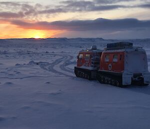 A Hägglunds heading along a snowy road into the sunrise