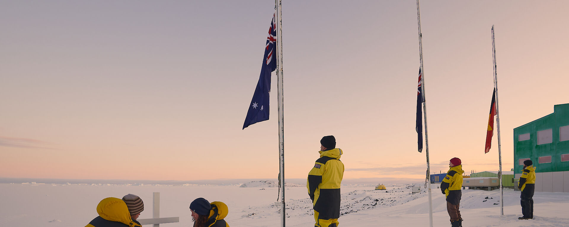 Expeditioners laying wreath at cross. Three flags half mast