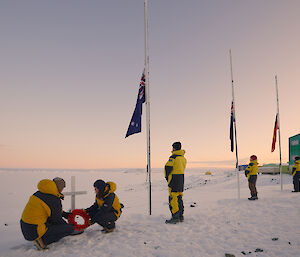 Expeditioners laying wreath at cross. Three flags half mast