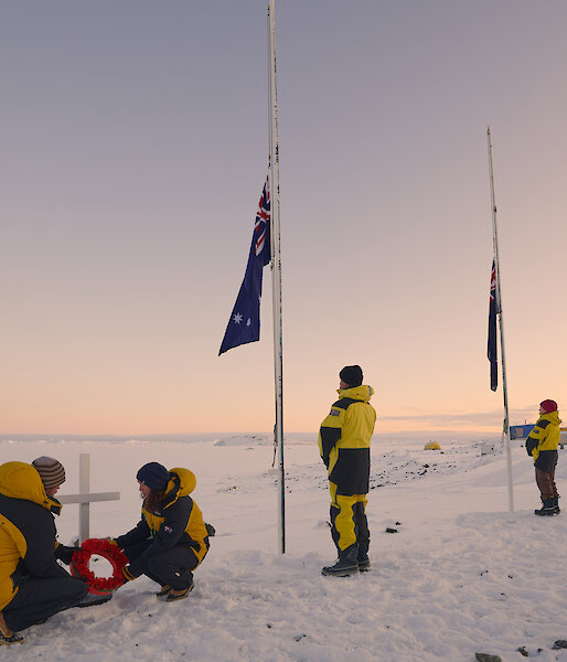 Expeditioners laying wreath at cross. Three flags half mast
