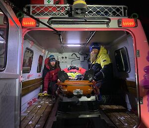 An expeditioner and the doctor sit next to casualty in the rear cabin of the pink Hägglunds