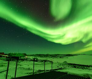 A burst of bright green aurora streaks across the sky above a sleepy Davis station