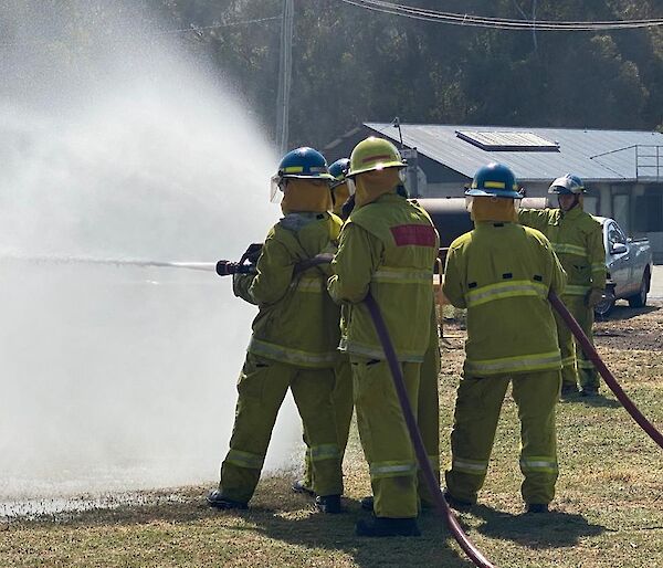 Three expeditioners using a fire hose at training