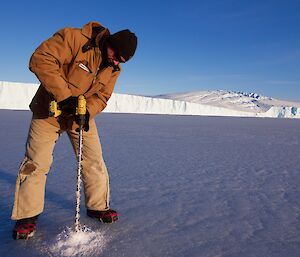 an expeditioner drilling into the sea ice