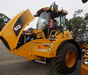 A yellow tip truck with its engine bay uncovered.