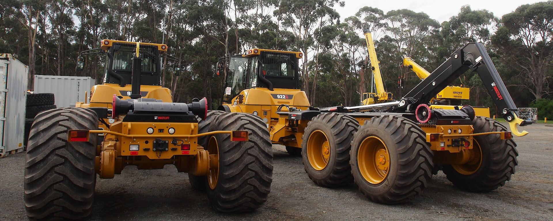 The rear view of two tip trucks. One has its hydraulic hook deployed towards the back of the vehicle.