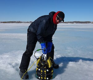 A scientist holding a remotely operated vehicle above a hole in the sea ice.