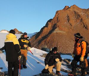 Four expeditioners standing on the ice in front of a mountain ridge