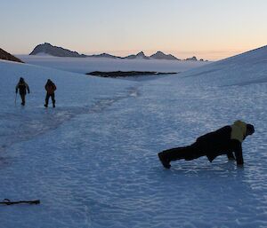 Two expeditioners walk by a man doing push ups on the ice