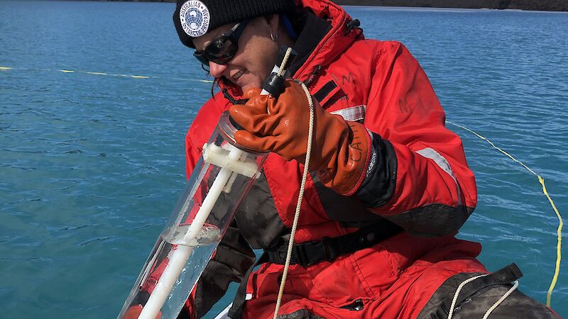 Scientist sampling water from an Antarctic lake in an inflatable rubber boat.